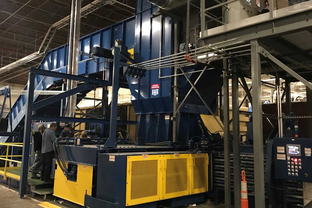 Blue And Yellow Harris American Co. Baler Indoors Being Inspected By Employees
